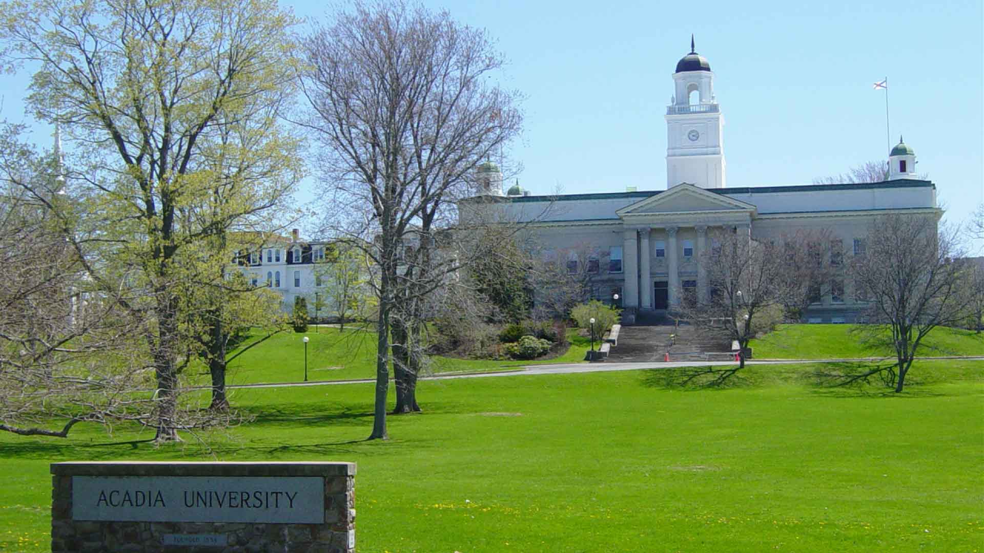 Acadia University sign in front of University Hall with large grass field and blue sky