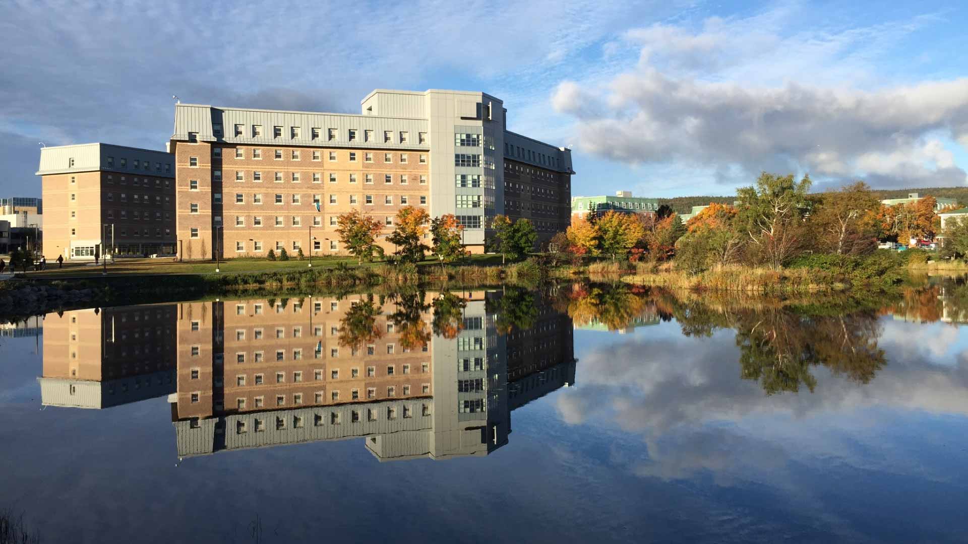Memorial University of Newfloundand building under blue sky reflecting in the water